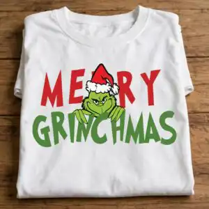 merry grinchmas png design with the grinch and santa hat a green furry creature wearing a Santa hat, peeking over green text, with red text above design printed on a plain product mo
