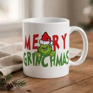 merry grinchmas png design with the grinch and santa hat a green furry creature wearing a Santa hat, peeking over green text, with red text above design printed on a plain product mo