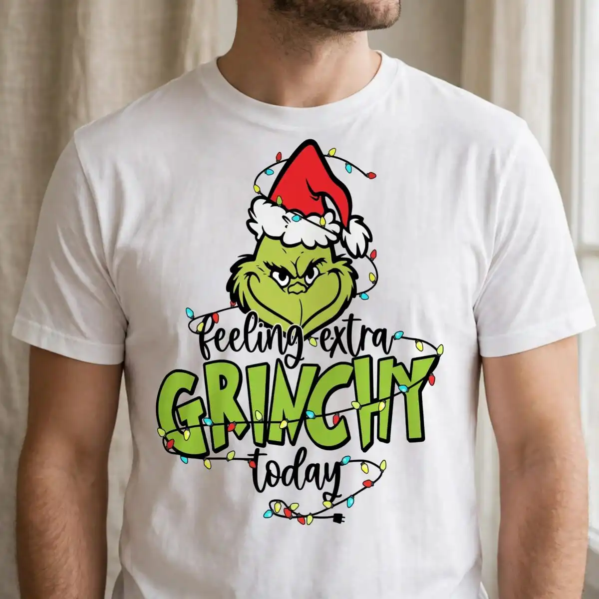 A green character wearing a Santa hat, surrounded by Christmas lights and text. design printed on a plain product mockup