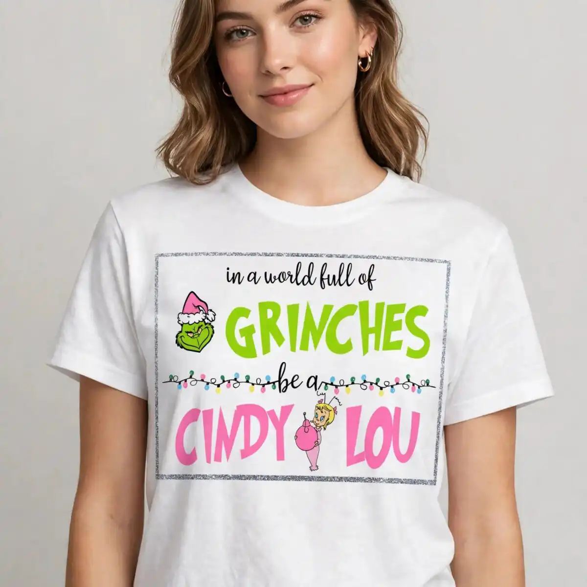 a quote about being kind with a green character wearing a Santa hat and a small girl holding an ornament, framed by glitter d